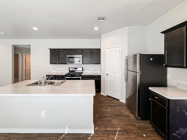 kitchen with a center island with sink, sink, a textured ceiling, dark hardwood / wood-style flooring, and stainless steel appliances