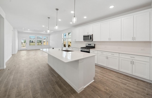 kitchen with decorative light fixtures, stainless steel appliances, light countertops, white cabinets, and a sink