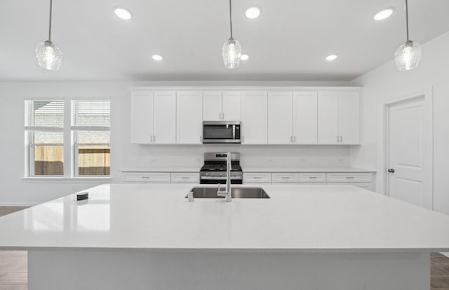 kitchen featuring stainless steel appliances, an island with sink, a sink, and pendant lighting