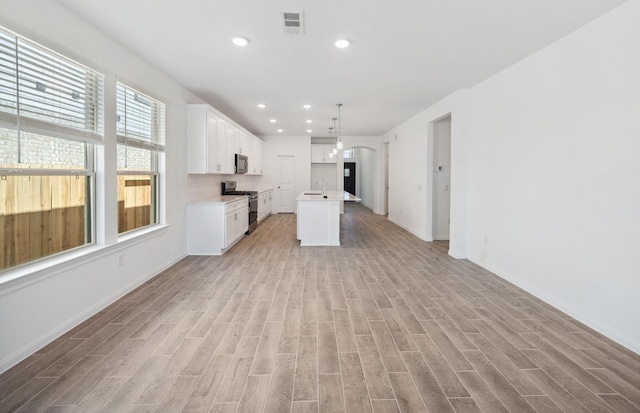 kitchen with white cabinets, open floor plan, appliances with stainless steel finishes, an island with sink, and pendant lighting