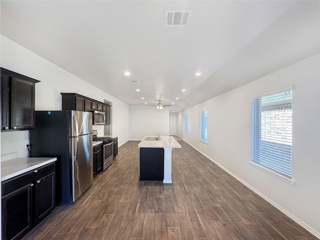 kitchen with ceiling fan, sink, stainless steel appliances, dark hardwood / wood-style floors, and a kitchen island with sink