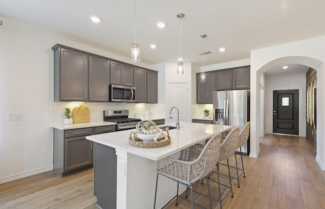 kitchen featuring a center island with sink, hanging light fixtures, light hardwood / wood-style floors, a kitchen bar, and stainless steel appliances