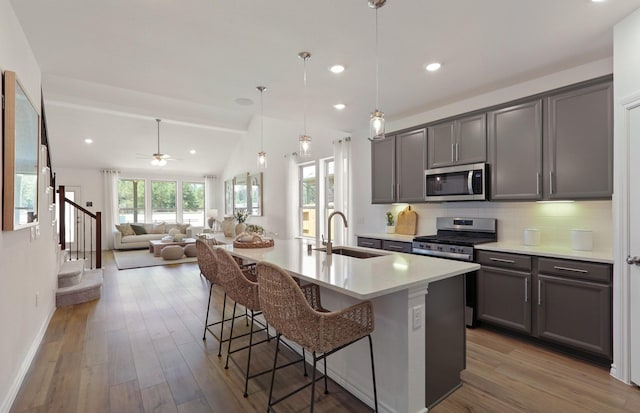 kitchen with sink, stainless steel appliances, a breakfast bar area, a kitchen island with sink, and light wood-type flooring