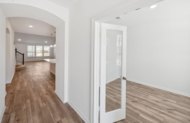 hallway featuring light wood-type flooring, arched walkways, visible vents, and stairway