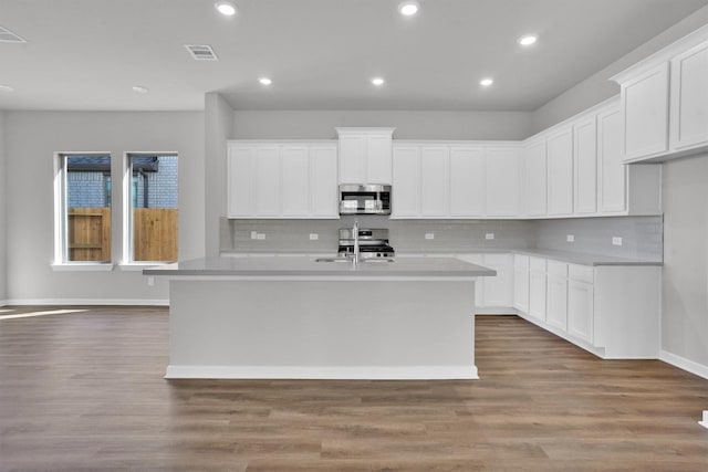 kitchen with appliances with stainless steel finishes, backsplash, a center island with sink, hardwood / wood-style flooring, and white cabinets