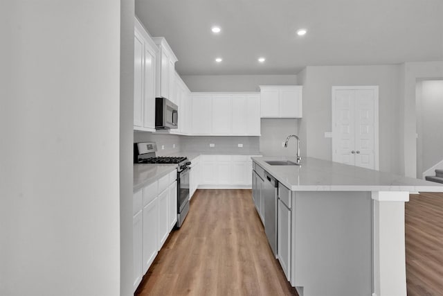 kitchen with sink, stainless steel appliances, light hardwood / wood-style floors, a center island with sink, and white cabinets