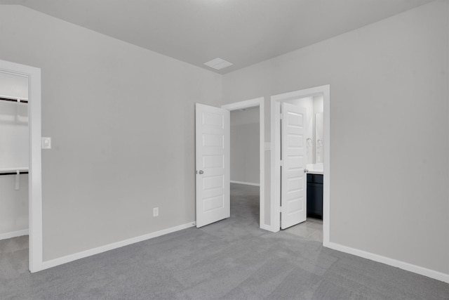 unfurnished bedroom featuring light carpet, connected bathroom, a spacious closet, and a closet