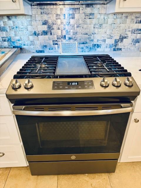 interior details with tasteful backsplash, white cabinetry, and stainless steel gas range oven