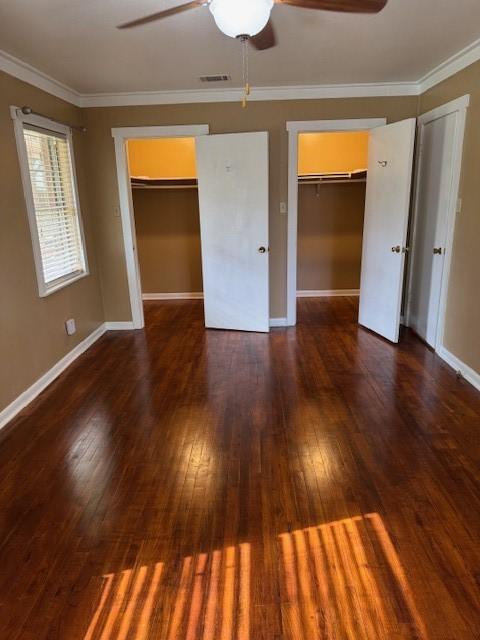 unfurnished bedroom featuring ceiling fan, crown molding, dark wood-type flooring, and two closets