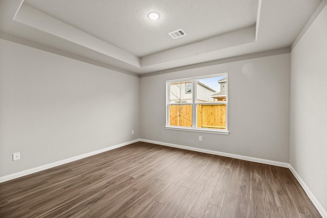 spare room featuring a raised ceiling, wood-type flooring, and a textured ceiling