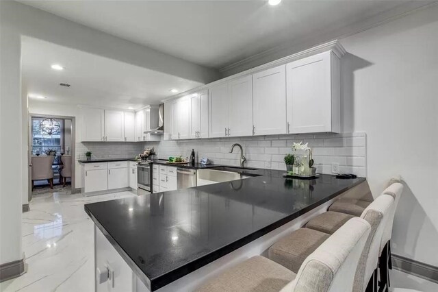 kitchen with white cabinetry, stainless steel appliances, wall chimney range hood, kitchen peninsula, and a kitchen bar