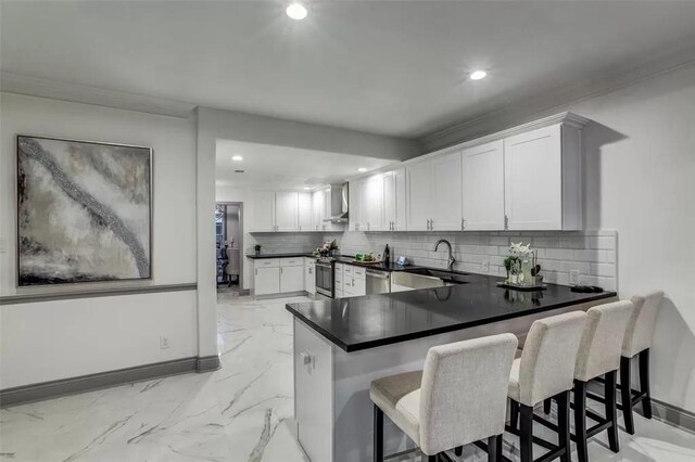 kitchen featuring kitchen peninsula, a kitchen breakfast bar, appliances with stainless steel finishes, wall chimney exhaust hood, and white cabinetry