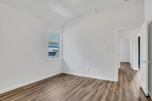 spare room featuring wood-type flooring and vaulted ceiling