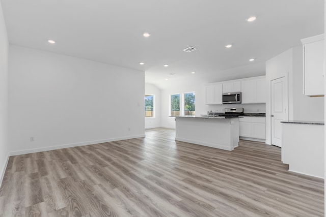 kitchen with stainless steel appliances, white cabinetry, light hardwood / wood-style floors, and an island with sink