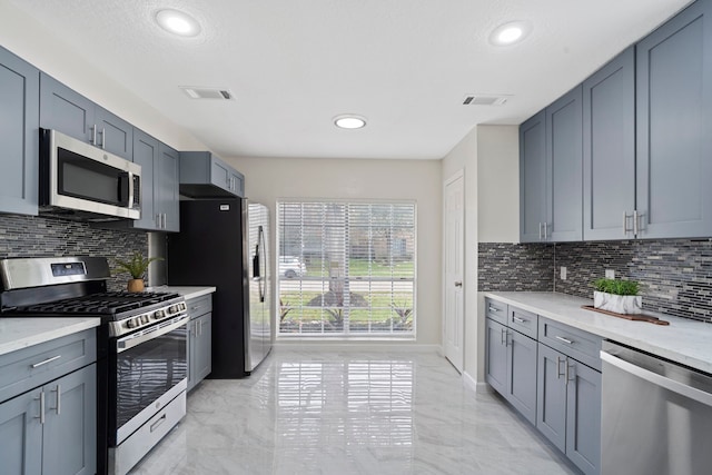 kitchen featuring tasteful backsplash, light stone counters, a textured ceiling, and appliances with stainless steel finishes