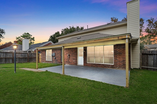 back house at dusk featuring a lawn and a patio area