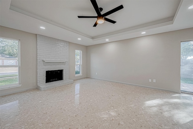 unfurnished living room featuring ceiling fan, a raised ceiling, and a brick fireplace