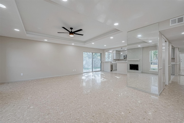 unfurnished living room featuring a fireplace, a raised ceiling, ceiling fan, and sink