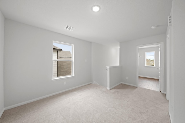 spare room with light colored carpet, visible vents, and baseboards