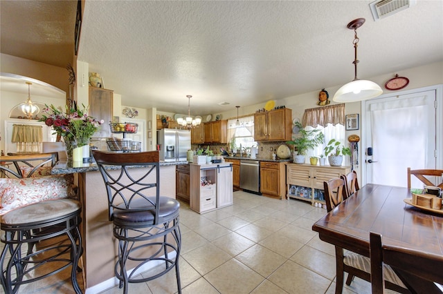 kitchen with kitchen peninsula, appliances with stainless steel finishes, a textured ceiling, pendant lighting, and a notable chandelier