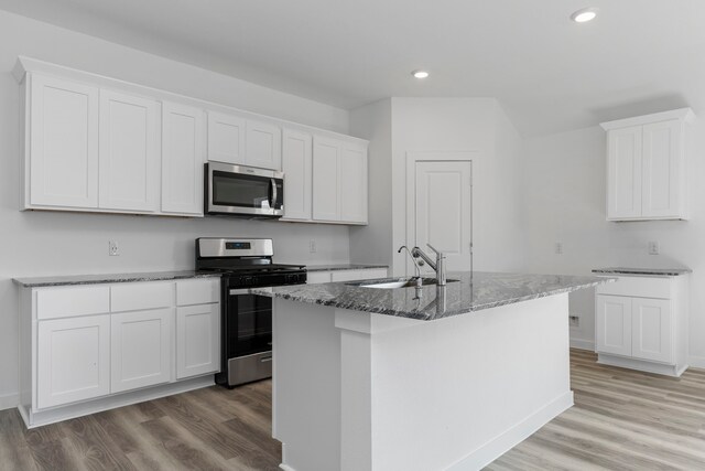 kitchen with white cabinetry, sink, stainless steel appliances, dark stone counters, and a center island with sink