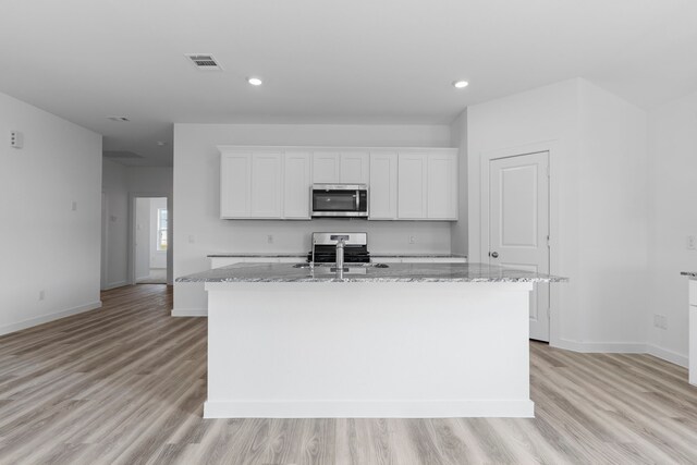 kitchen with light stone countertops, appliances with stainless steel finishes, light wood-type flooring, a center island with sink, and white cabinetry