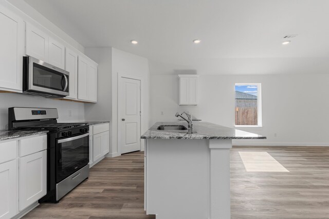 kitchen featuring white cabinetry, sink, stainless steel appliances, an island with sink, and light hardwood / wood-style floors