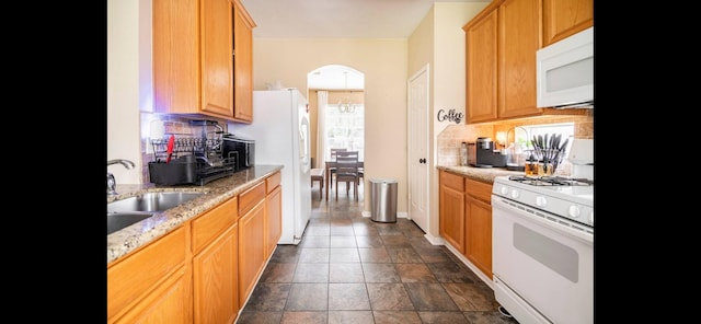 kitchen with backsplash, light stone counters, white appliances, and sink