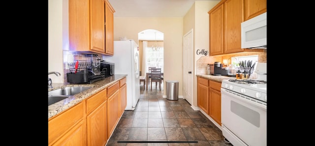 kitchen featuring decorative backsplash, white appliances, light stone counters, and sink