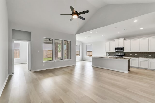 kitchen featuring white cabinets, light wood-type flooring, an island with sink, tasteful backsplash, and stainless steel appliances