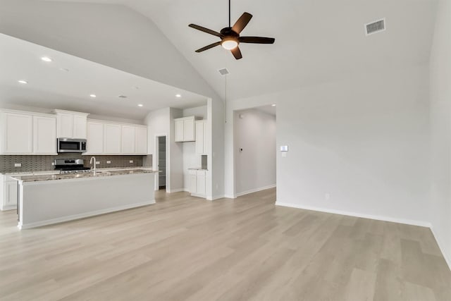 kitchen with light stone counters, high vaulted ceiling, a center island with sink, white cabinets, and appliances with stainless steel finishes