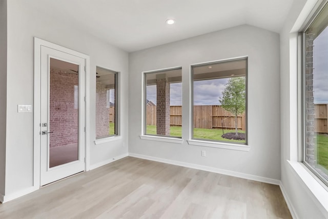 unfurnished room featuring plenty of natural light, light hardwood / wood-style floors, and vaulted ceiling