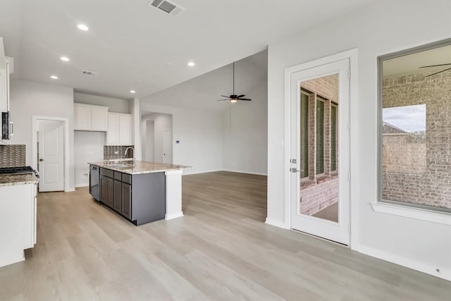 kitchen with light wood-type flooring, tasteful backsplash, a kitchen island with sink, sink, and white cabinetry