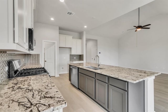 kitchen with light stone counters, stainless steel appliances, sink, a center island with sink, and white cabinets