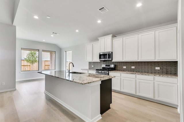 kitchen with light stone countertops, stainless steel appliances, sink, white cabinetry, and an island with sink