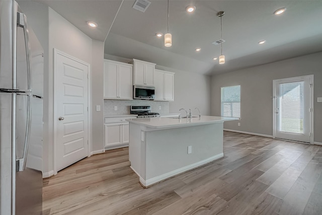 kitchen with appliances with stainless steel finishes, light wood-type flooring, white cabinetry, and a kitchen island with sink