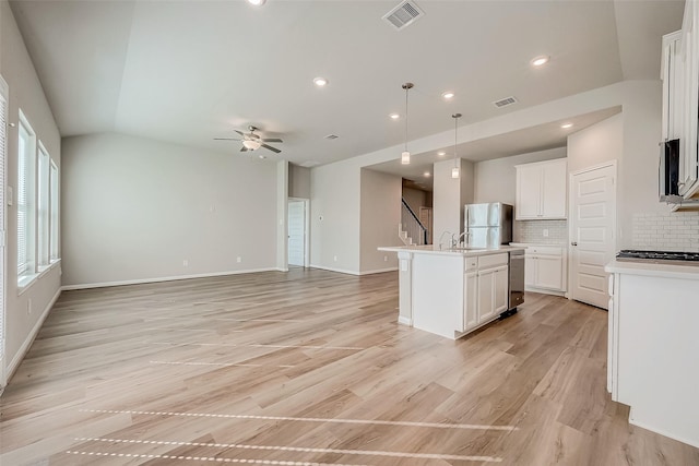 kitchen featuring appliances with stainless steel finishes, light wood-type flooring, pendant lighting, and an island with sink