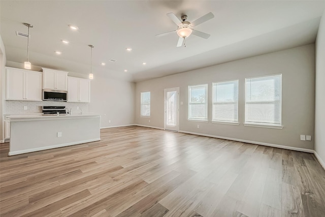 unfurnished living room featuring plenty of natural light, ceiling fan, and light hardwood / wood-style flooring