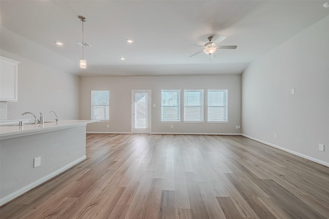 unfurnished living room with ceiling fan, sink, and light wood-type flooring