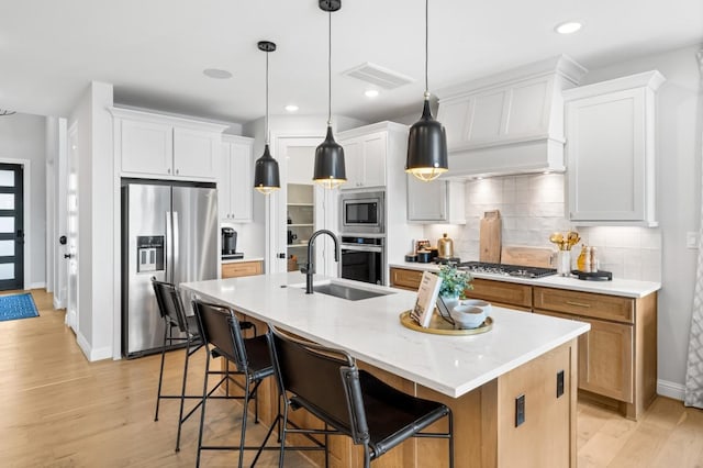 kitchen featuring appliances with stainless steel finishes, a center island with sink, white cabinetry, and pendant lighting