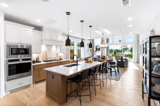 kitchen with stainless steel appliances, a sink, white cabinetry, light countertops, and a center island with sink