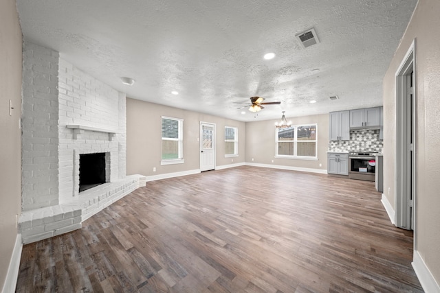 unfurnished living room featuring dark wood-type flooring, a textured ceiling, and a brick fireplace