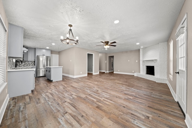 unfurnished living room featuring a brick fireplace, a textured ceiling, wood-type flooring, and ceiling fan with notable chandelier