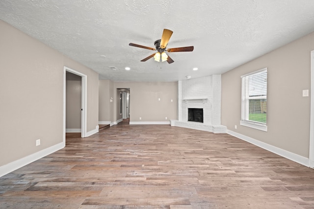 unfurnished living room with ceiling fan, light hardwood / wood-style floors, a textured ceiling, and a brick fireplace