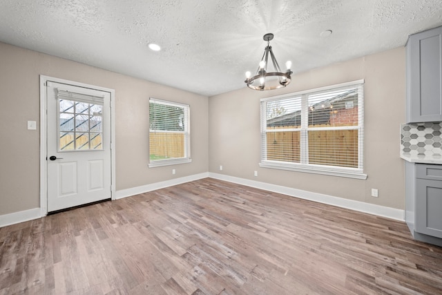 unfurnished dining area with an inviting chandelier, light hardwood / wood-style floors, and a textured ceiling