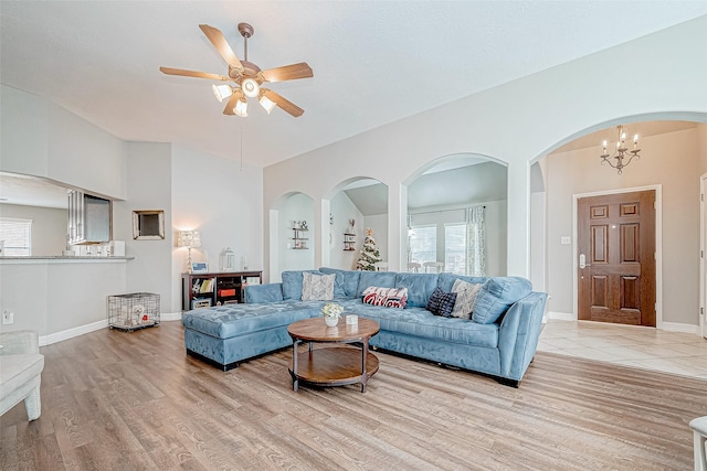 living room with ceiling fan with notable chandelier, light hardwood / wood-style floors, and vaulted ceiling