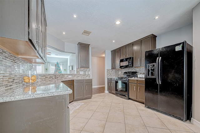 kitchen featuring decorative backsplash, light tile patterned floors, light stone counters, and black appliances