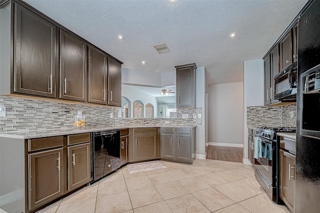 kitchen with light stone countertops, ceiling fan, dark brown cabinets, light tile patterned floors, and black appliances