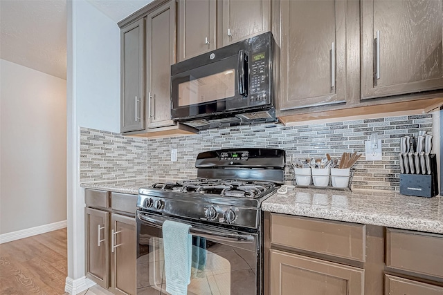 kitchen featuring tasteful backsplash, light stone counters, black appliances, and light hardwood / wood-style floors