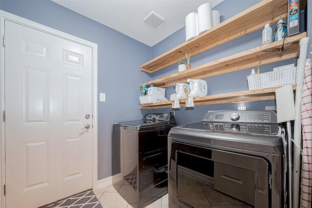 laundry area with light tile patterned floors, a textured ceiling, and washing machine and clothes dryer